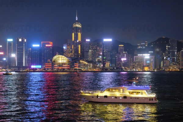 Hong Kong skyline cityscape downtown skyscrapers over Victoria Harbour in the evening illuminated with tourist boat ferries, Hong Kong, China, Asia