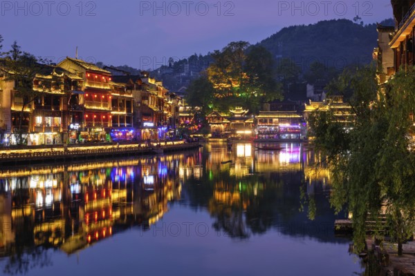 Chinese tourist attraction destination, Feng Huang Ancient Town (Phoenix Ancient Town) on Tuo Jiang River with bridge illuminated at night. Hunan Province, China, Asia
