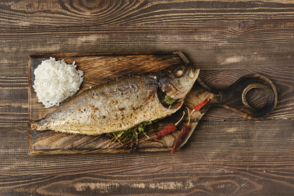 Yellow tailed mackerel with rice baked in oven on wooden cutting board, top view