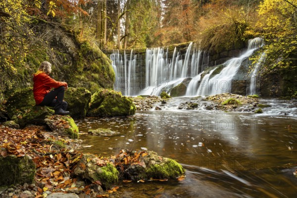 The Geratser waterfall in autumn. A hiker sits on a rock. Moss-covered rocks on the sides, trees in autumn leaves. Gerats, Upper Allgäu, Allgäu, Bavaria, Germany, Europe