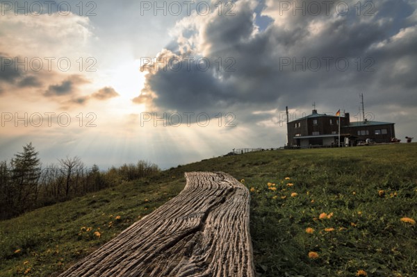 Simple bench in a meadow, illuminated by evening sun, sunbeams behind thunderclouds, mountain top with Köterberghaus, Köterberg, Lügde, Weserbergland, North Rhine-Westphalia, Germany, Europe