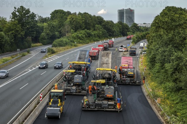 Essen, North Rhine-Westphalia, Germany, road construction, asphalt pavers and road rollers laying new, open-pored, whisper asphalt on the A52 motorway, here between the Essen-Kettwig and Essen-Rüttenscheid junctions in the direction of Dortmund. Skyline of Essen with the EON headquarters building in the background, Europe