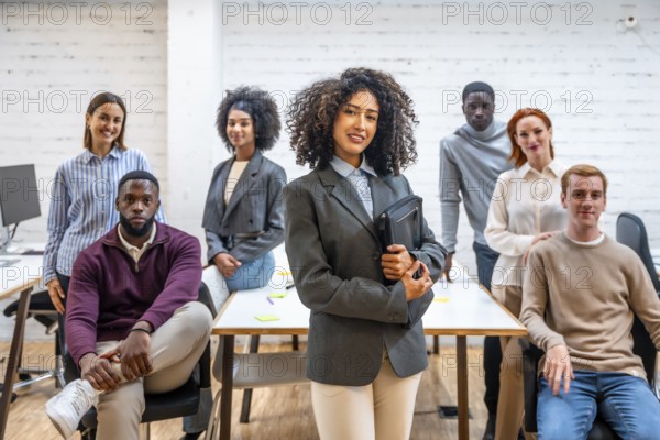 Female leader wirh business clothes and curly hair standing next to teamwork in a coworking