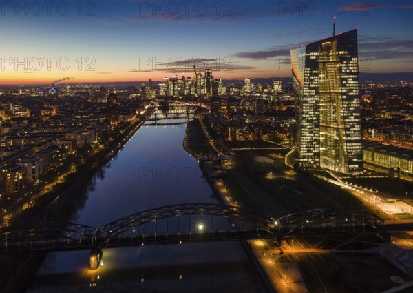 The lights in the offices of the European Central Bank (ECB) and in the skyscrapers of Frankfurt's banking skyline glow in the evening shortly after sunset. (Aerial view with a drone), Frankfurt am Main, Osthafen, Hesse, Germany, Europe