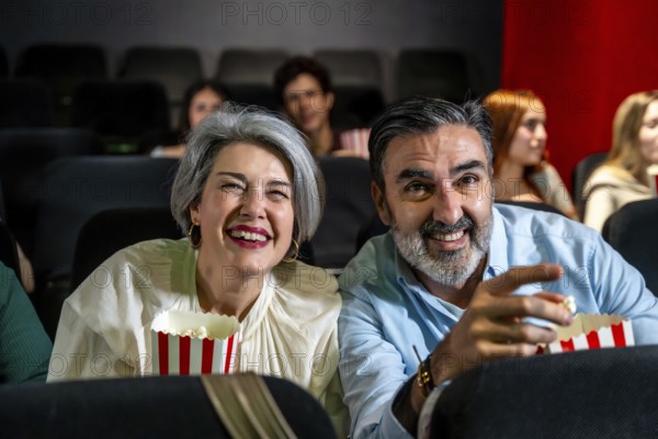 Happy mature couple laughing and having fun watching a movie at the cinema, eating popcorn