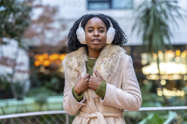 Fashionable young woman enjoys winter day in the city, wearing stylish earmuffs and a warm coat with fur collar