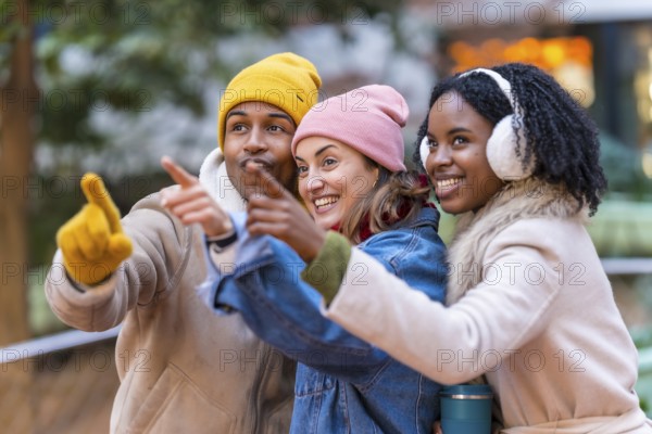 Three happy multi ethnic friends wearing winter clothes pointing their fingers at something interesting while walking in a city park