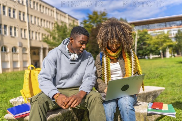 Multiracial students doing homework using laptop sitting outside the university sitting on a bench under the sun