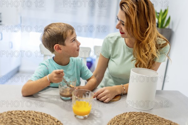 Schoolboy and mother dipping biscuits on milk enjoying breakfast before going to school
