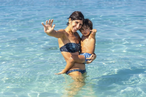 Mother holding her son and waving at estanys beach, enjoying summer holidays in mallorca, spain