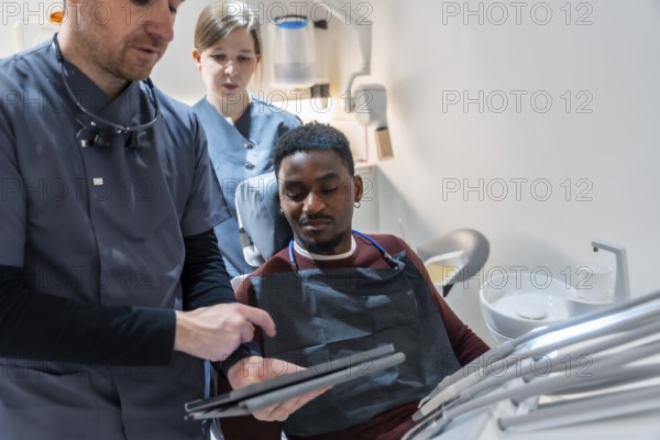 Dentist and nurse showing dental scan results on digital tablet to patient in modern clinic
