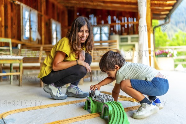 Mother and son enjoying quality time, playing with a toy train set on a rustic porch