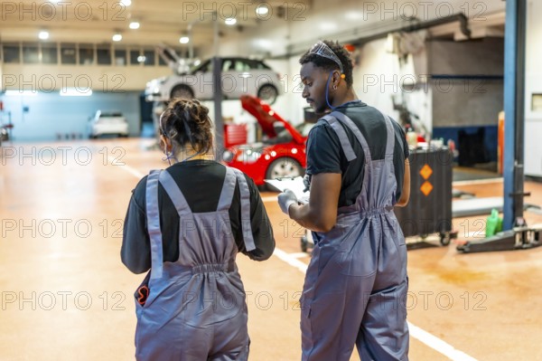 Two auto mechanics walking and reviewing notes on a clipboard in a professional garage, surrounded by vehicles on lifts