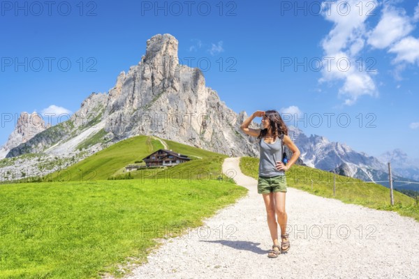 Female tourist enjoying summer vacation hiking in dolomites, italy, walking on path near mountain peak and alpine hut at giau pass