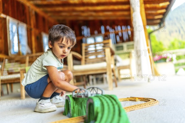Young boy playing with a toy train set on a porch of a wooden cabin