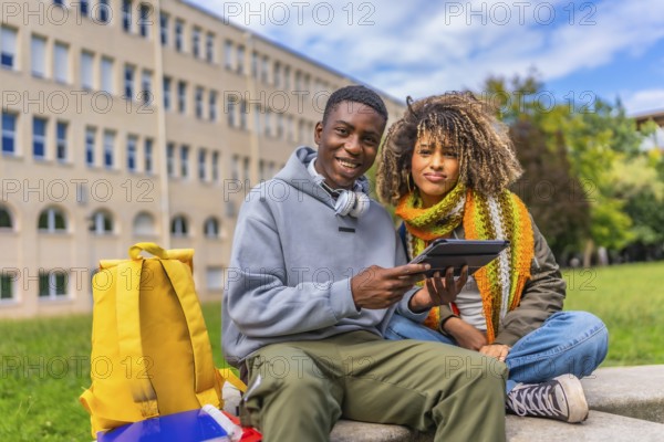 Diverse students smiling at camera while using tablet outside the university campus