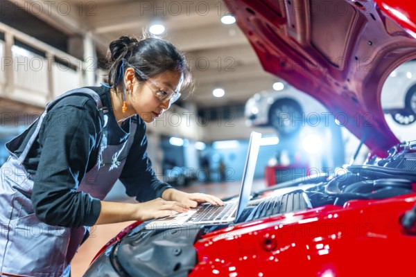 Young female mechanic using a laptop while inspecting a car engine in a professional auto repair shop