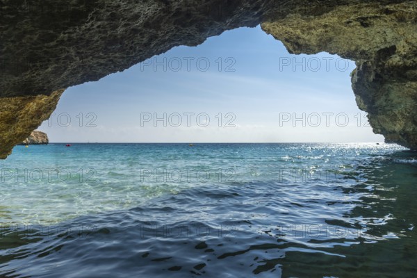 Crystal clear turquoise waters of the mediterranean sea glisten under the summer sun, viewed from inside a sea cave in cala domingos, mallorca