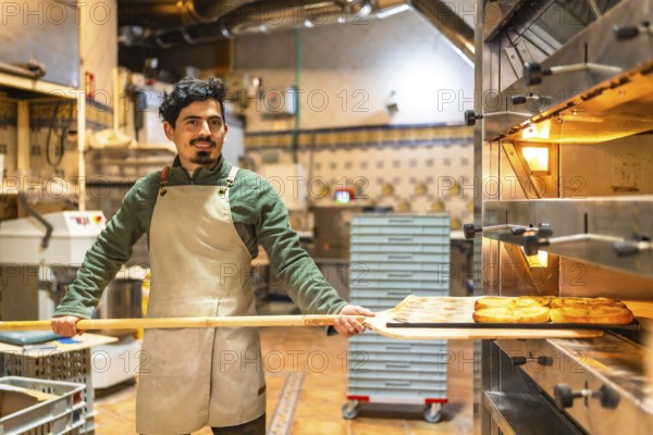 Male latin baker working removing tasty puff pastries from a traditional oven using peel
