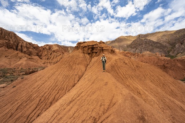 Mountaineer on a mountain ridge, eroded mountain landscape with sandstone rocks, canyon with red and orange rock formations, Konorchek Canyon, Chuy, Kyrgyzstan, Asia