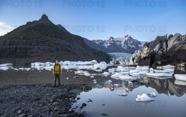 Hikers at a lake, reflection in the Svínafellslon glacier lagoon with ice floes, Svínasfellsjökull glacier tongue, glaciated mountain peak Hrútfjallstindar in the background, at sunset, Svínafell, Iceland, Europe