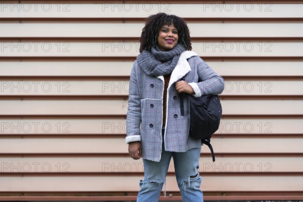 Portrait of black ethnic girl a gray wall in the university, with mochica from school on the back to school