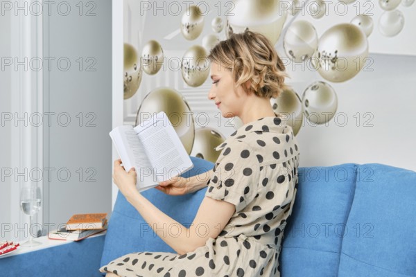 Barefoot woman sitting on sofa and reading the book, view ofrom the side