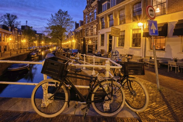 Typical Netherlands cityscape, bycicle at canal with boats and houses illuminated in the evening. Haarlem, Netherlands