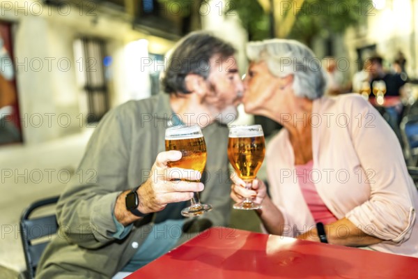 Senior couple kissing while toasting with beer in an outdoor terrace in the city