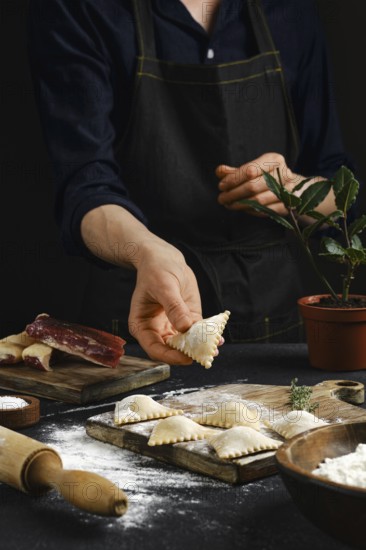 A person in an apron carefully shapes filled pasta in a warmly lit kitchen. Flour dust covers the countertop as various ingredients are arranged nearby, highlighting the process of handmade cooking.