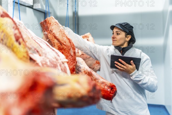 Female butcher using digital tablet to analyze products in a cold meat storage room