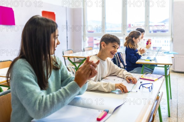Happy elementary school students clapping hands in classroom, enjoying learning and having fun at school