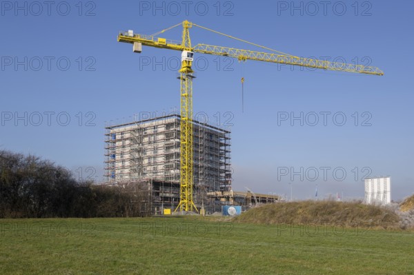 Building under construction behind overgrown hill, with crane and clear sky, residential construction, new construction of 50 flats, new development area, apartment building, construction site, Winnenden, Baden-Württemberg, Germany, Europe