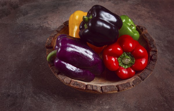 A collection of colorful bell peppers, in a wooden bowl, on a dark surface, top view, no people