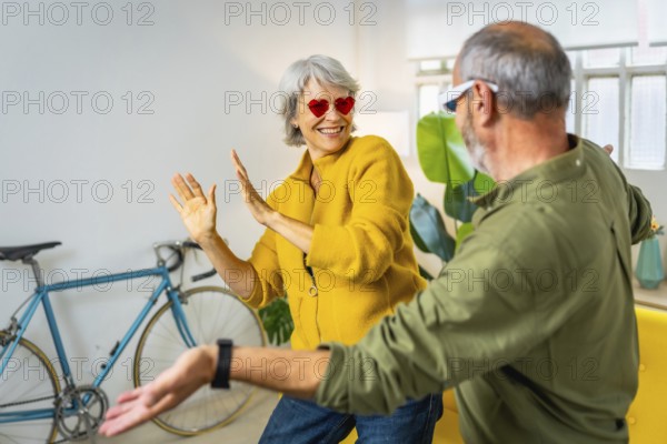 Modern senior couple with stylish sunglasses having fun together at home laughing and dancing