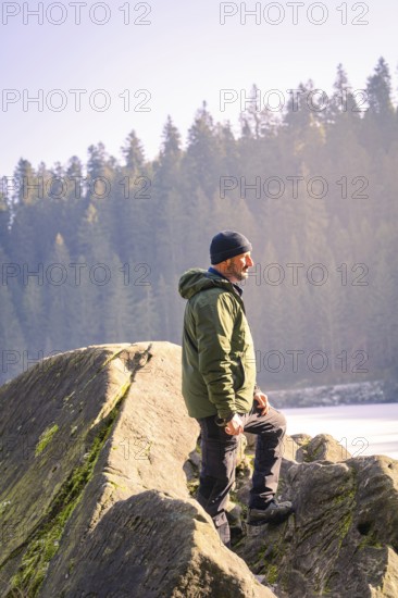 Man with outdoor clothes standing on a rock, surrounded by forest and sunlight, Glaswaldsee, Bad Rippoldsau-Schapbach, district of Wolfach, Black Forest, Germany, Europe