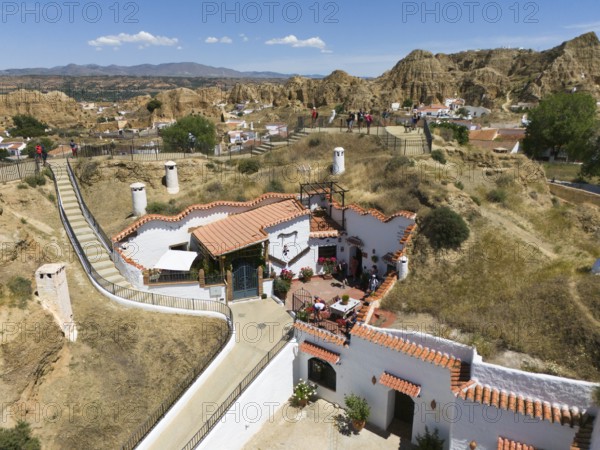 A white house with terracotta roof on a hill surrounded by nature and some people enjoying the scenery, aerial view, cave dwellings, cave neighbourhood, Troglodytos, Guadix, Granada, Andalusia, Spain, Europe