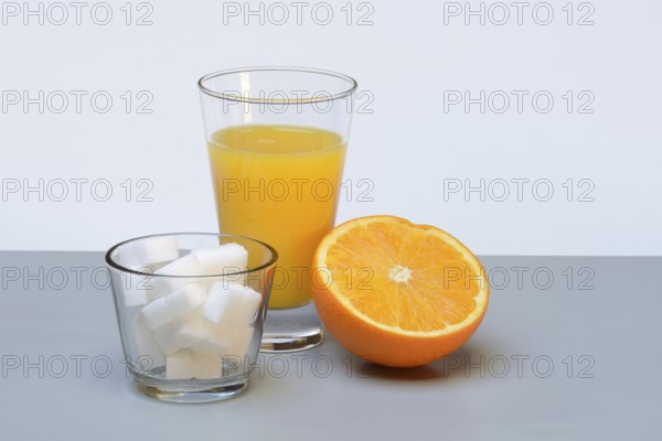 Orange juice in a drinking glass, half an orange and sugar cubes