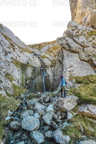 Hiker in blue jacket navigating rocky landscape near a small waterfall on mount txindoki, showcasing the rugged beauty of gipuzkoa, basque country
