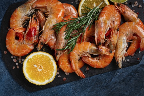 Freshly frozen shrimp, with lemon and rosemary, on black slate, close-up, top view, no people