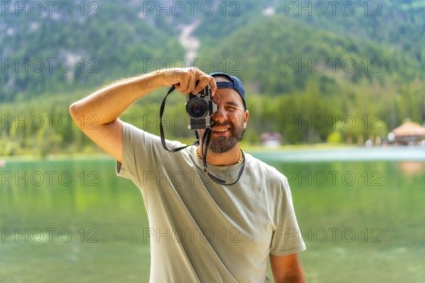 Tourist taking pictures with vintage camera at lake dobbiaco, surrounded by the breathtaking scenery of the dolomites in summer