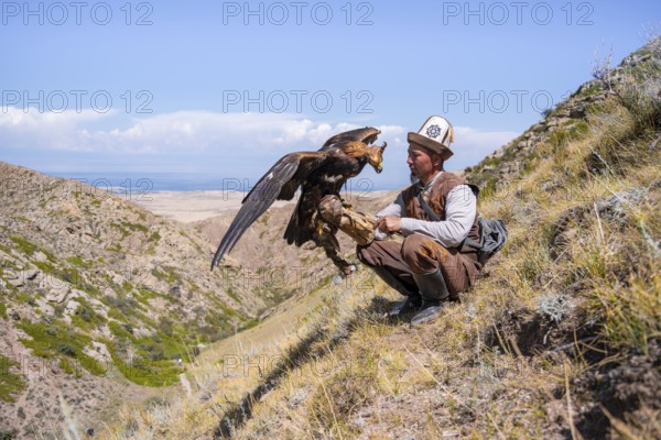 Traditional Kyrgyz eagle hunter with eagle in the mountains, near Kysyl-Suu, Kyrgyzstan, Asia