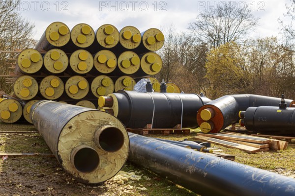 Stacked district heating pipes with yellow ends lie piled up in a meadow