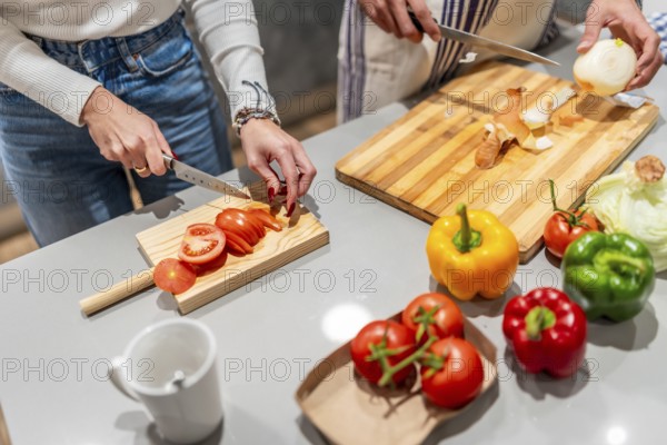 Two chefs slicing fresh tomatoes and onions on wooden cutting boards, surrounded by colorful bell peppers in a modern kitchen
