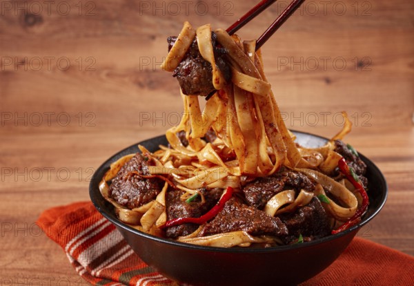 Udon noodles with beef in Mongolian style, with green onions and vegetables, served in a black bowl, on a wooden table, homemade, no people