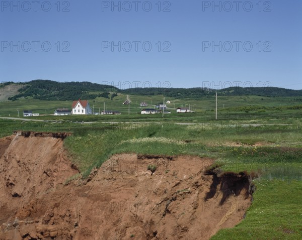 Cliff with eroded soil and houses in the distance in summer, Havre-Aubert, Magdalen Islands, Quebec, Canada, North America