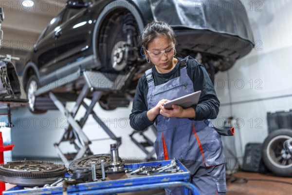 Young woman mechanic using a digital tablet, inspecting car parts and components in a professional workshop, ensuring efficient vehicle maintenance