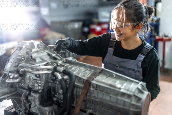 Asian woman mechanic working diligently on a vehicle gearbox in a professional garage, showcasing skill and expertise in automotive repair