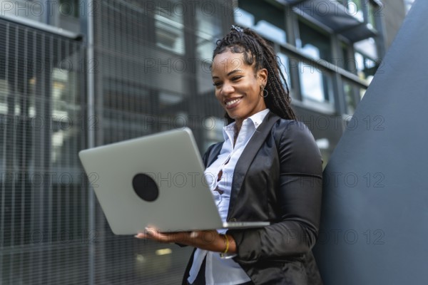 Hispanic confident businesswoman working with laptop standing outside a modern building