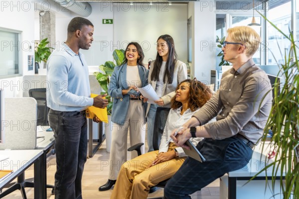 Five coworkers are discussing a project, sharing ideas and documents, in a modern coworking office
